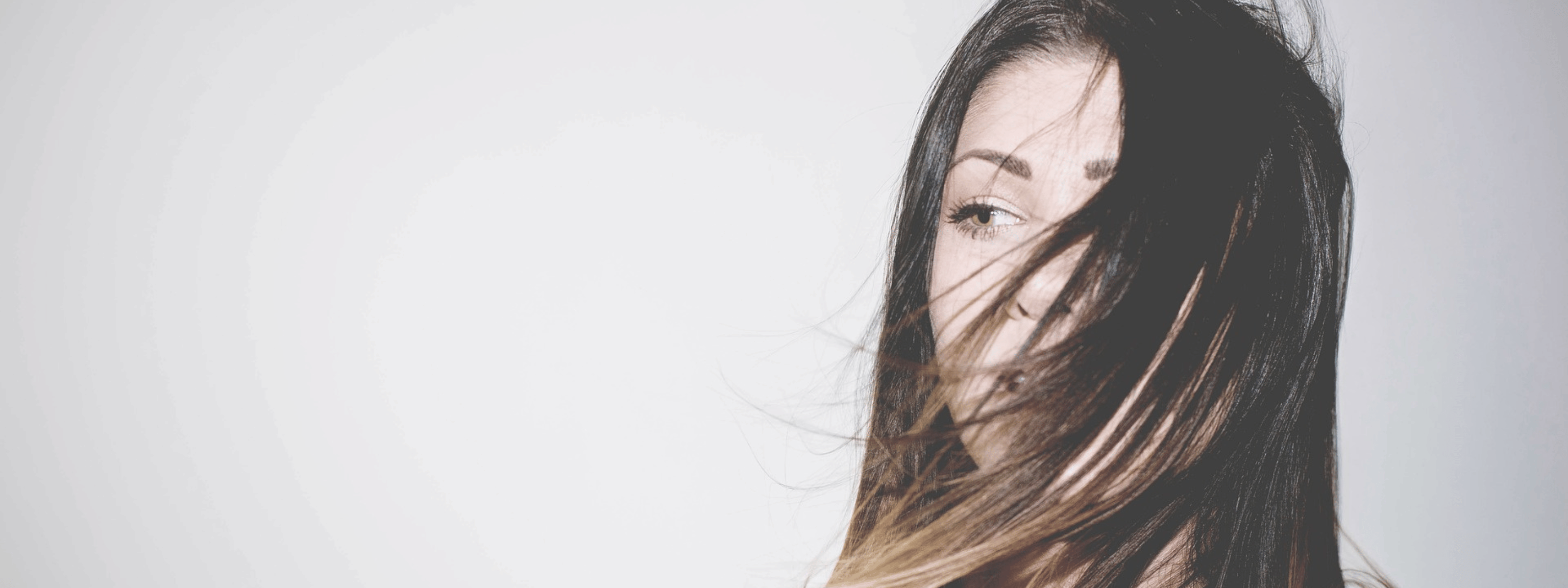 Woman with long brown hair partly covering her face, hair blowing gently, showcasing healthy, natural hair