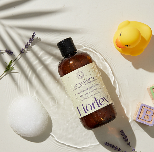 Fiorley baby bottle surrounded by bubbles, rubber ducky, and wooden letter blocks – natural baby shampoo