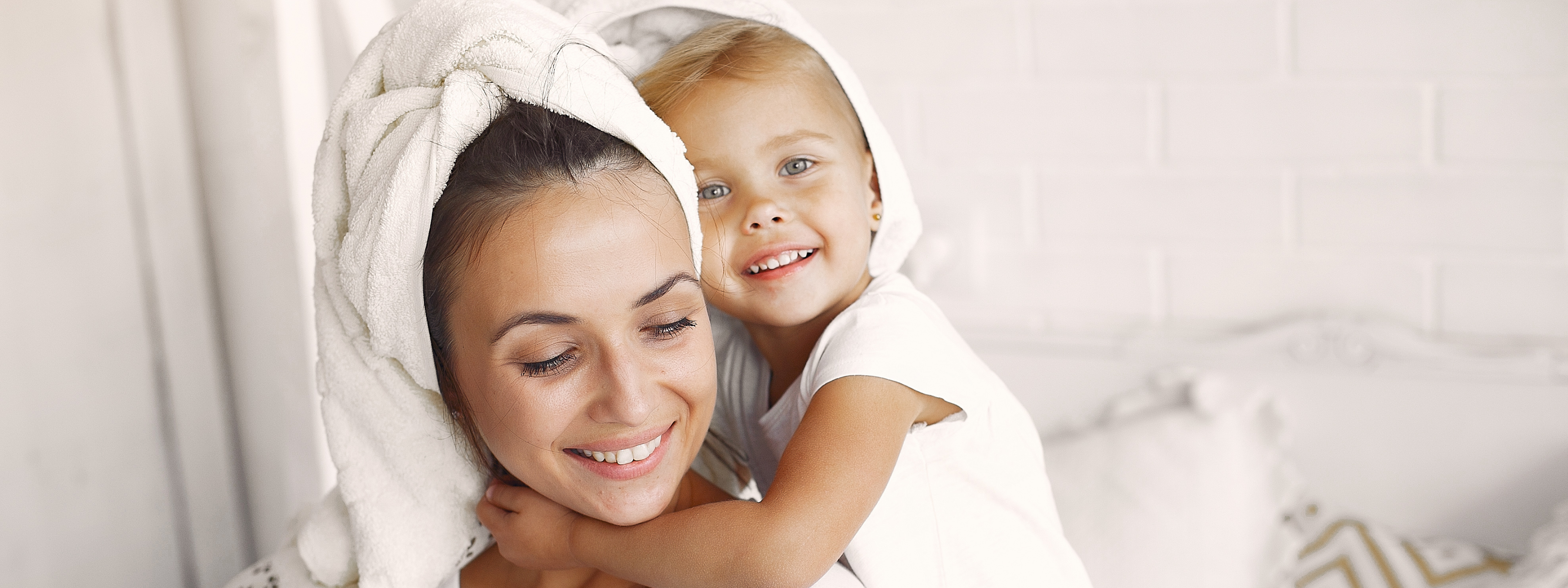 Toddler hugging mum around the neck, both smiling and wearing towels on head after a hair wash.